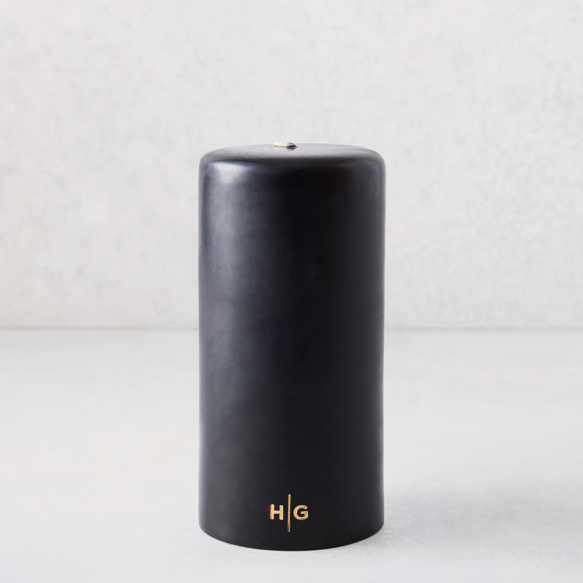 4x8 inch black hand-dipped pillar candle with gold HG logo and cotton wick.