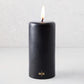 4x8 inch black unscented pillar candle with a burning wick and gold HG logo embossed on the base.