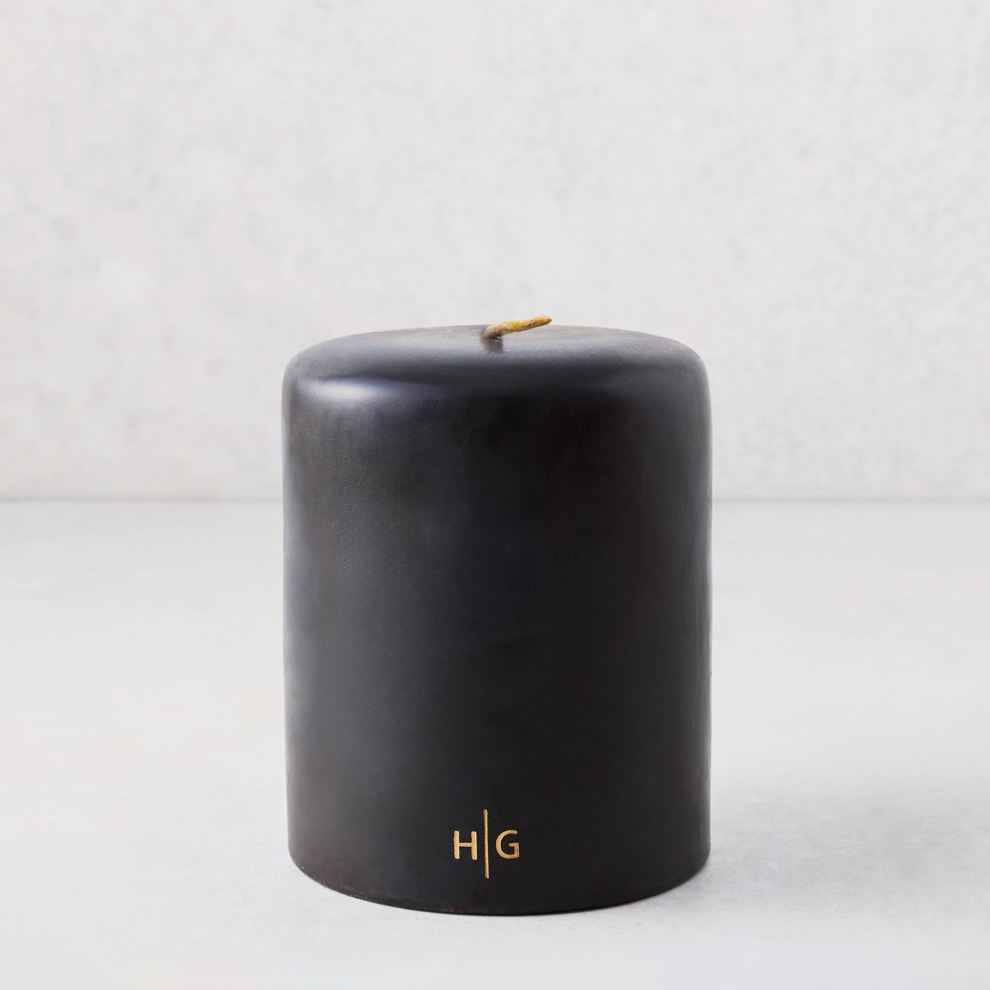5x6 inch black hand-dipped pillar candle with gold HG logo and cotton wick.