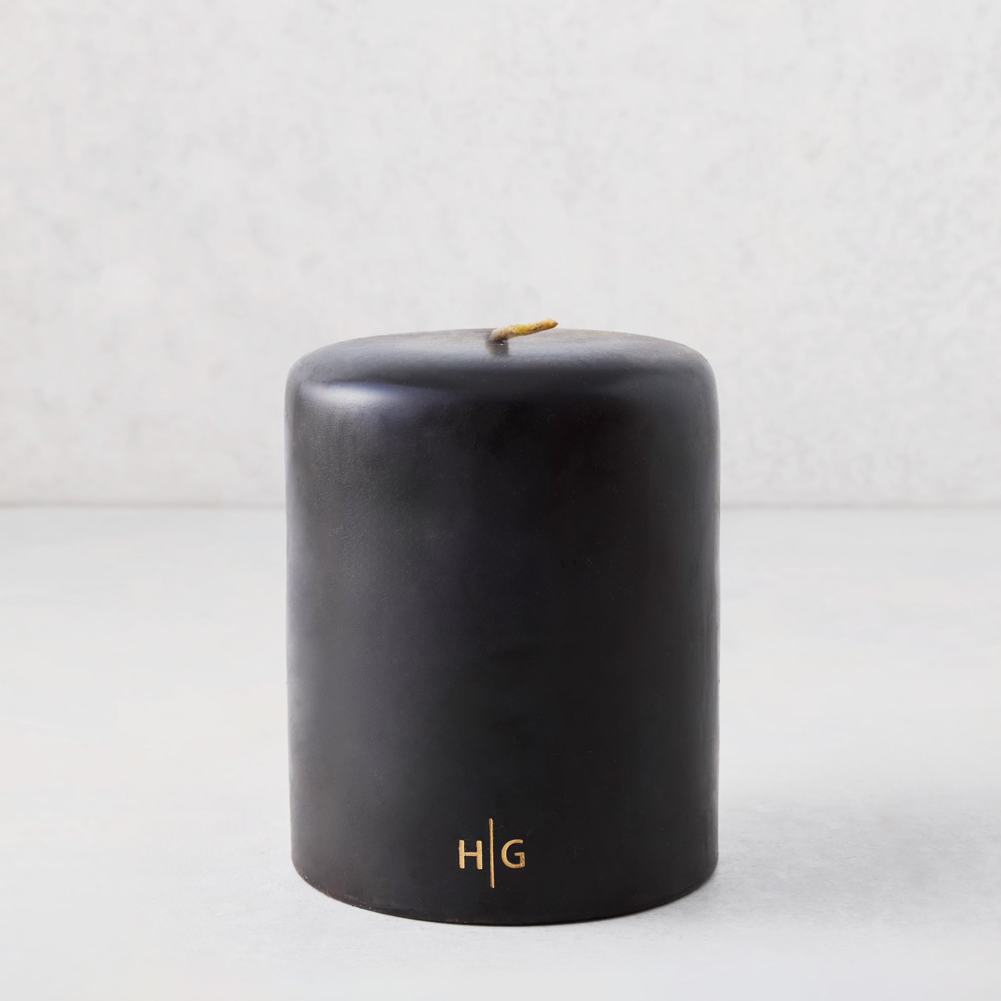 5x6 inch black hand-dipped pillar candle with gold HG logo and cotton wick.