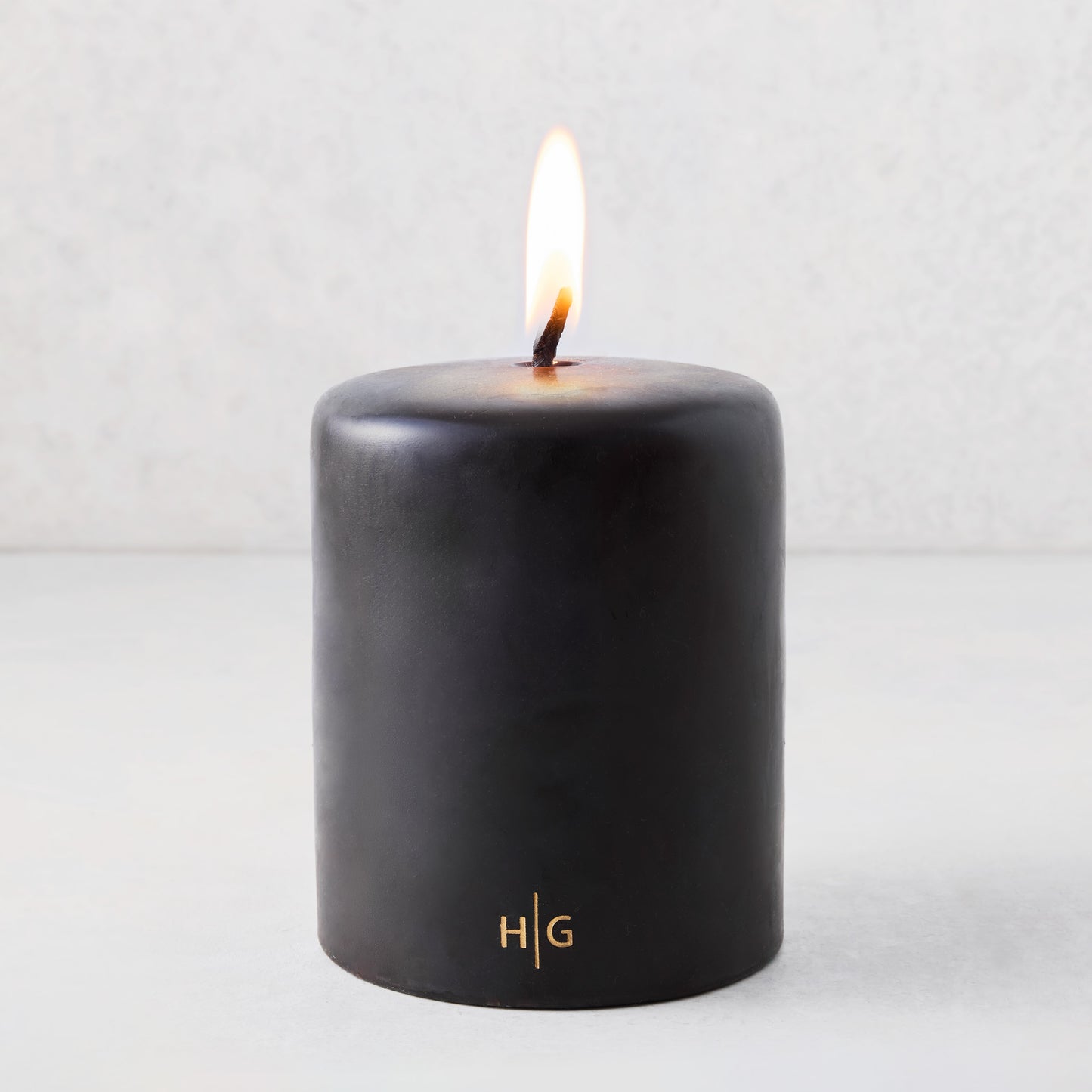5x6 inch black hand-dipped pillar candle with a burning wick and gold HG logo on a light gray background.