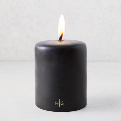 5x6 inch black hand-dipped pillar candle with a burning wick and gold HG logo on a light gray background.