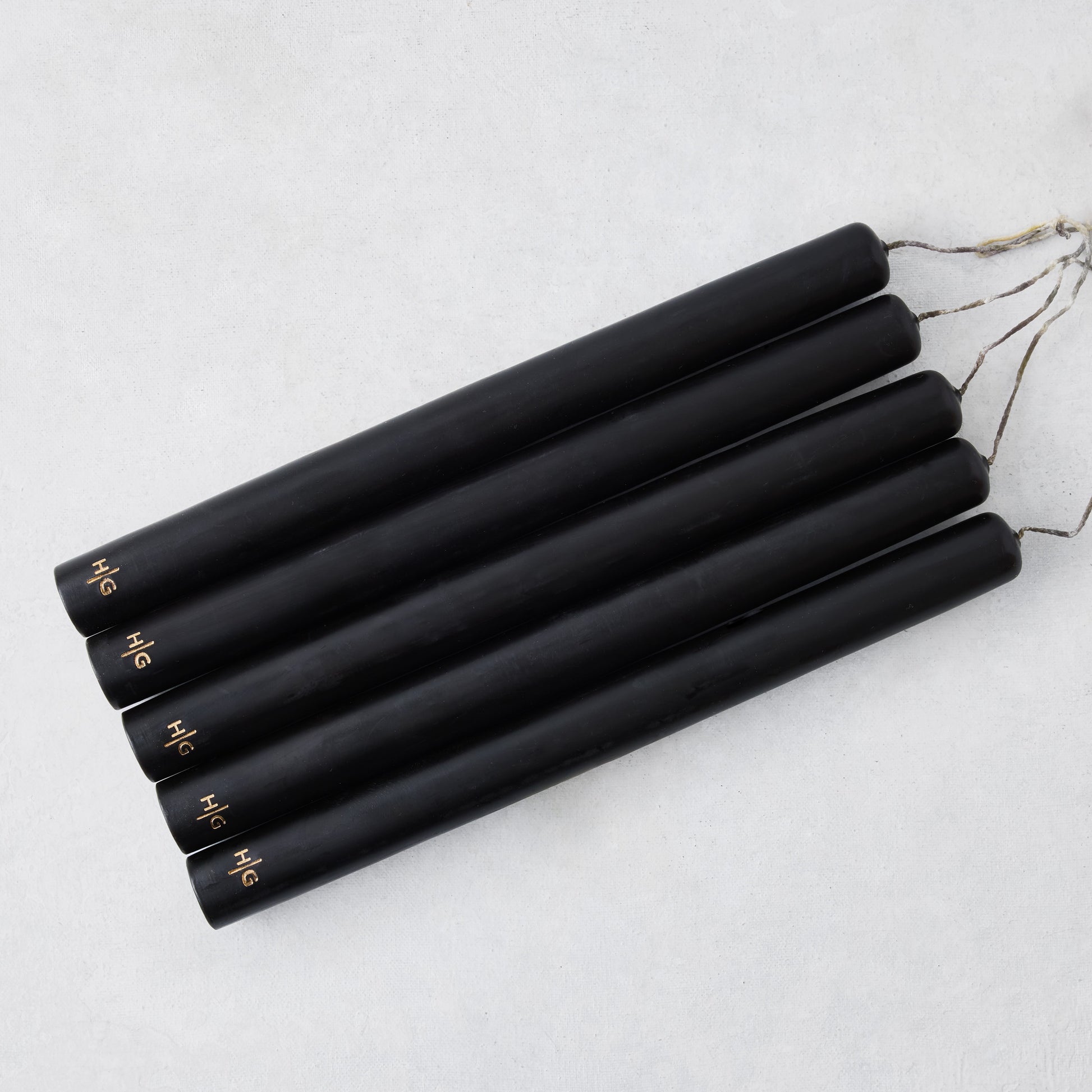 Set of five 10-inch black unscented taper candles with hand-embossed gold Hudson Grace logos on a white background.