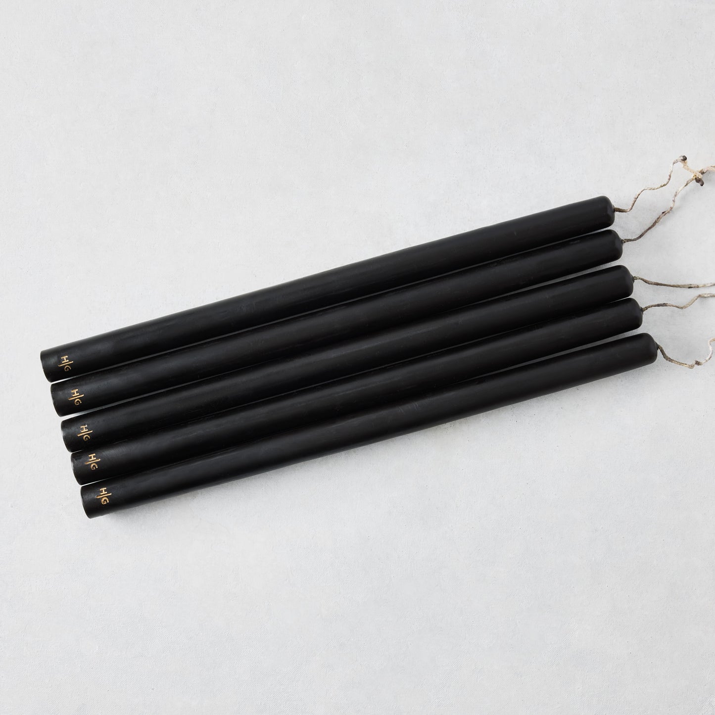Set of five 15-inch black hand-dipped taper candles with gold HG logo and cotton wicks on a white background.