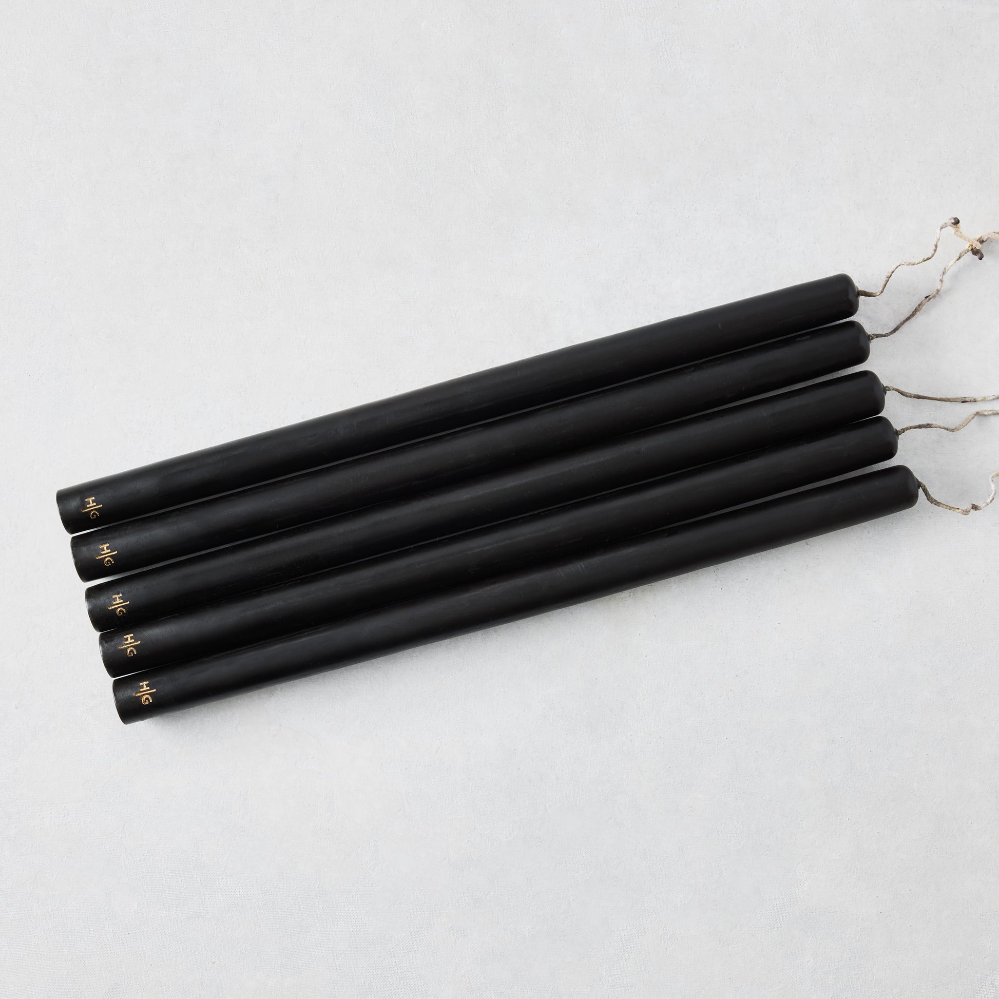 Set of five 15-inch black hand-dipped taper candles with gold HG logo and cotton wicks on a white background.