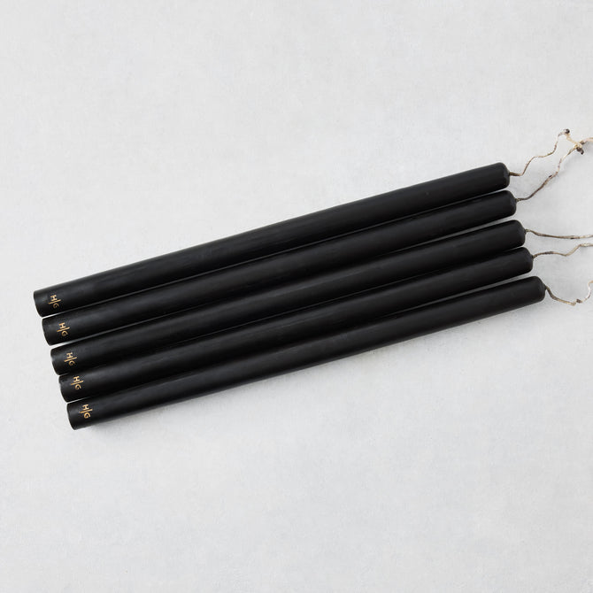 Set of five 15-inch black hand-dipped taper candles with gold HG logo and cotton wicks on a white background.