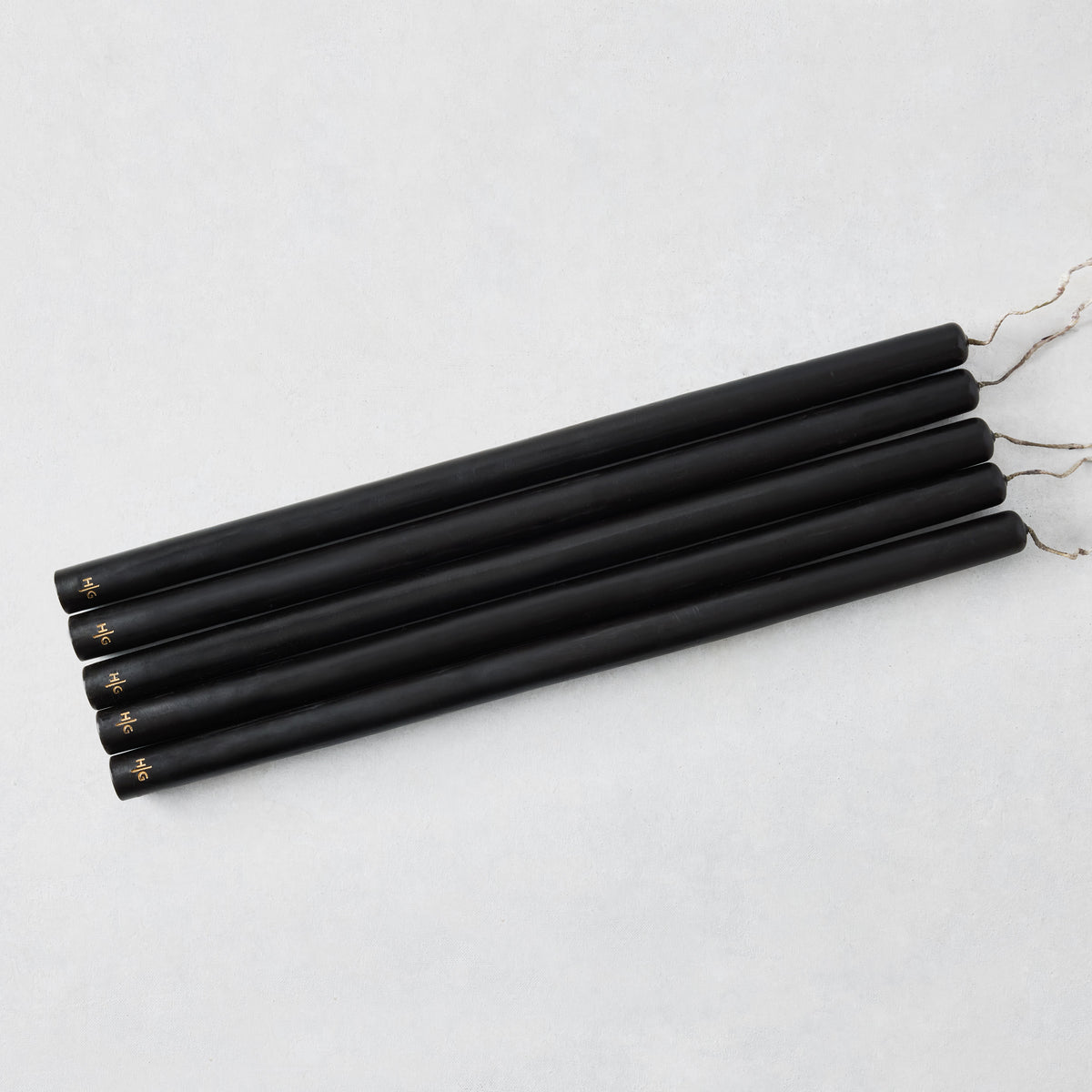 Set of five 17-inch hand-dipped black unscented taper candles with gold HG logo detail on a white background.