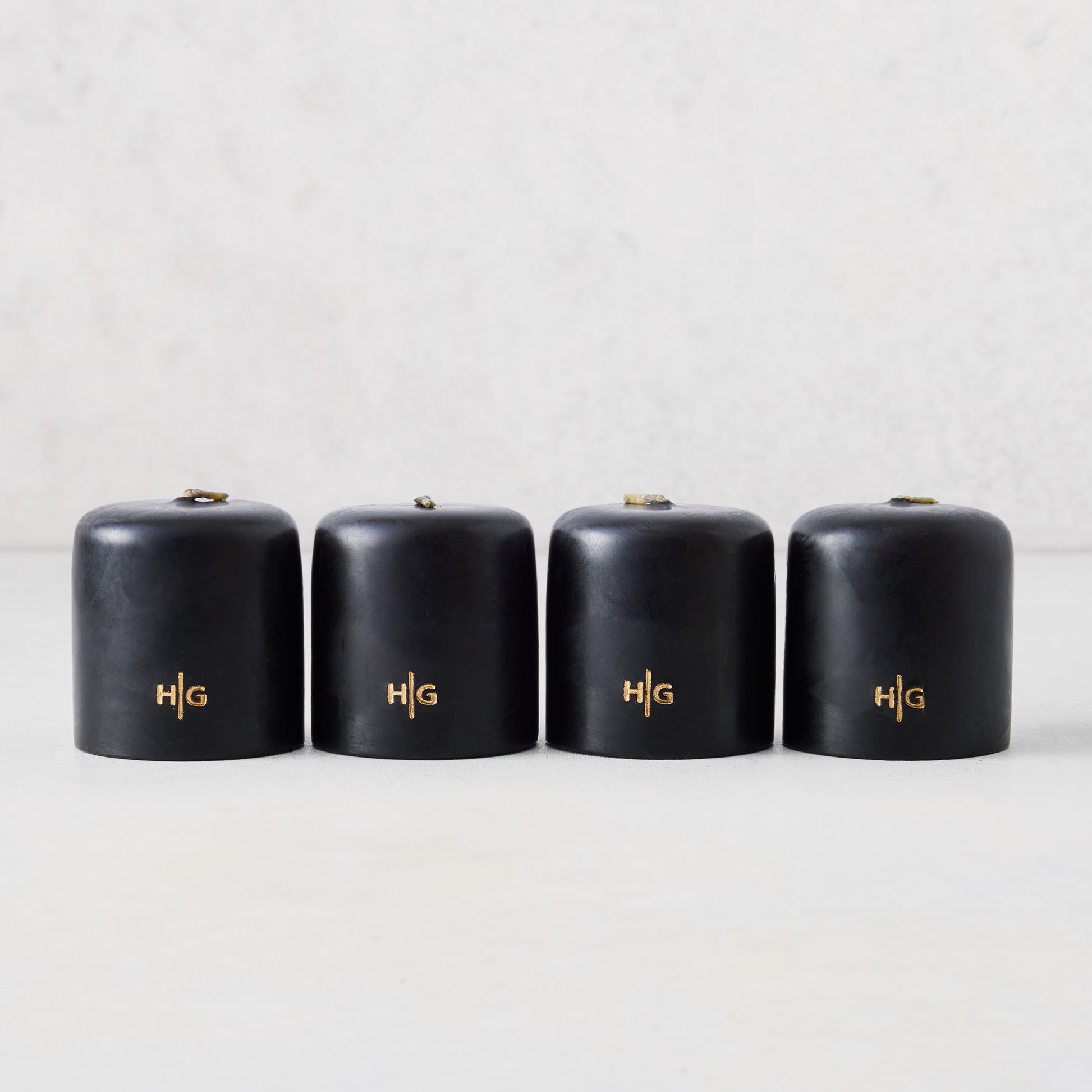 Set of four 2-inch black unscented votive candles with a gold embossed HG logo on a light background.