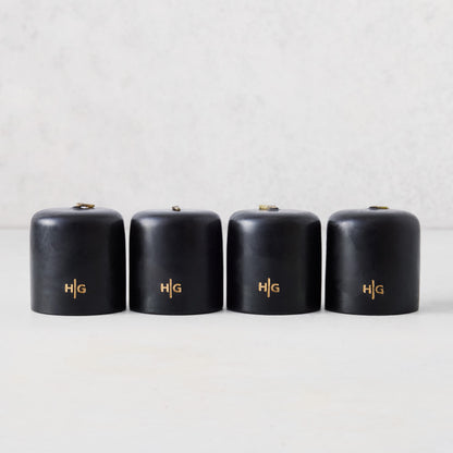 Set of four 2-inch black unscented votive candles with a gold embossed HG logo on a light background.
