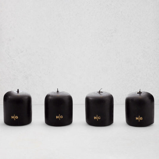 Four black unscented 2" votive candles with gold HG logo, made from paraffin and amber tree resin.