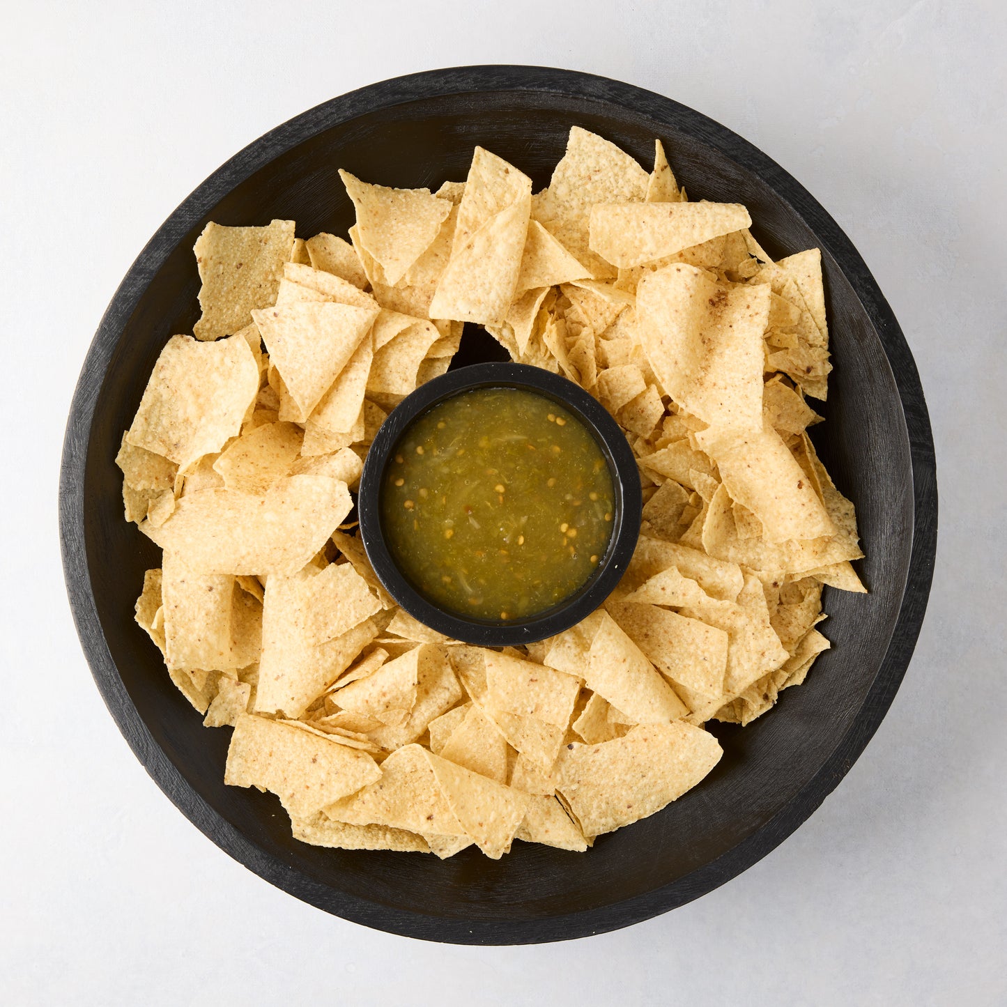 Black mango wood chip and dip platter with tortilla chips and green salsa.