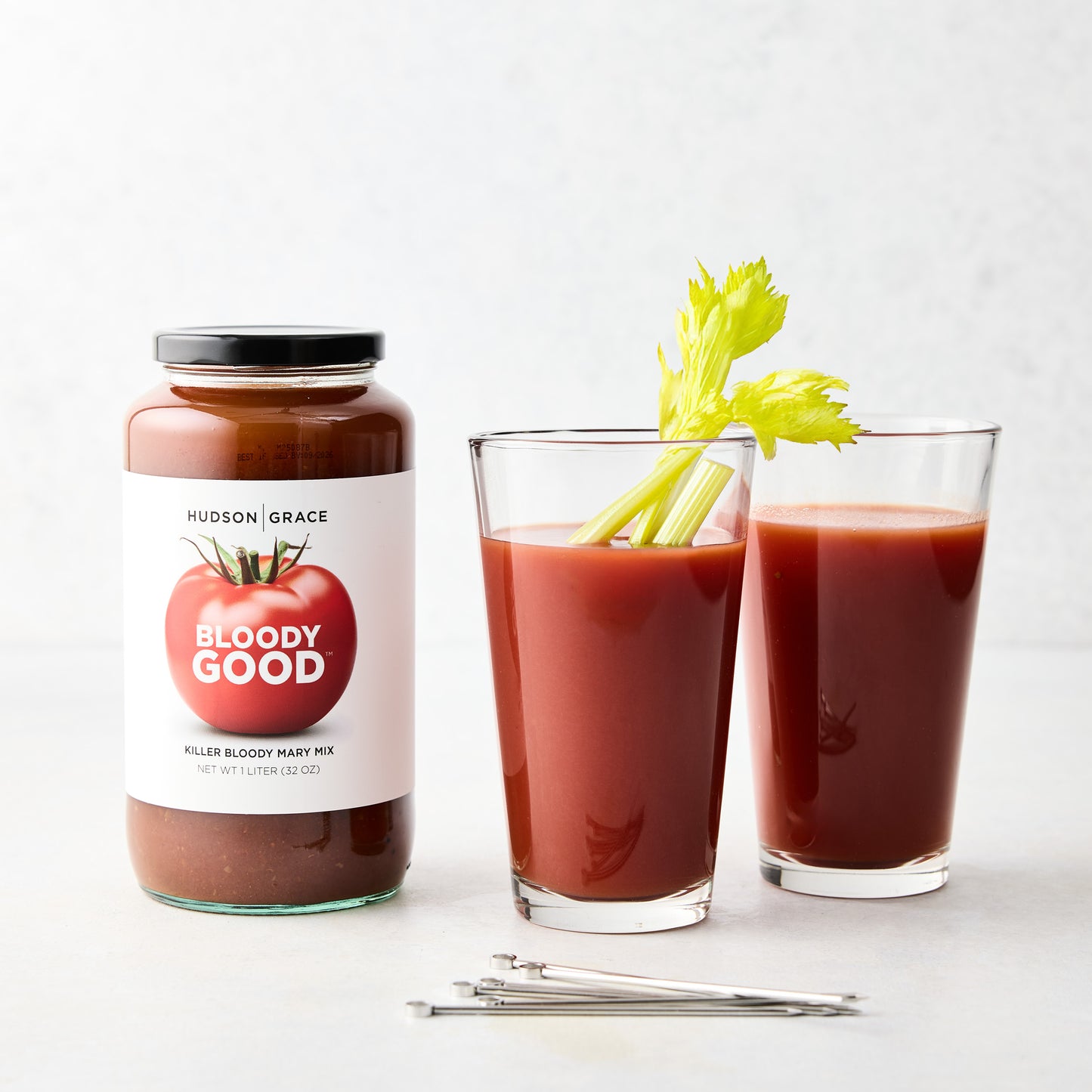 Hudson Grace "Bloody Good" Bloody Mary mix jar, two glasses with mix and celery, and silver cocktail picks.