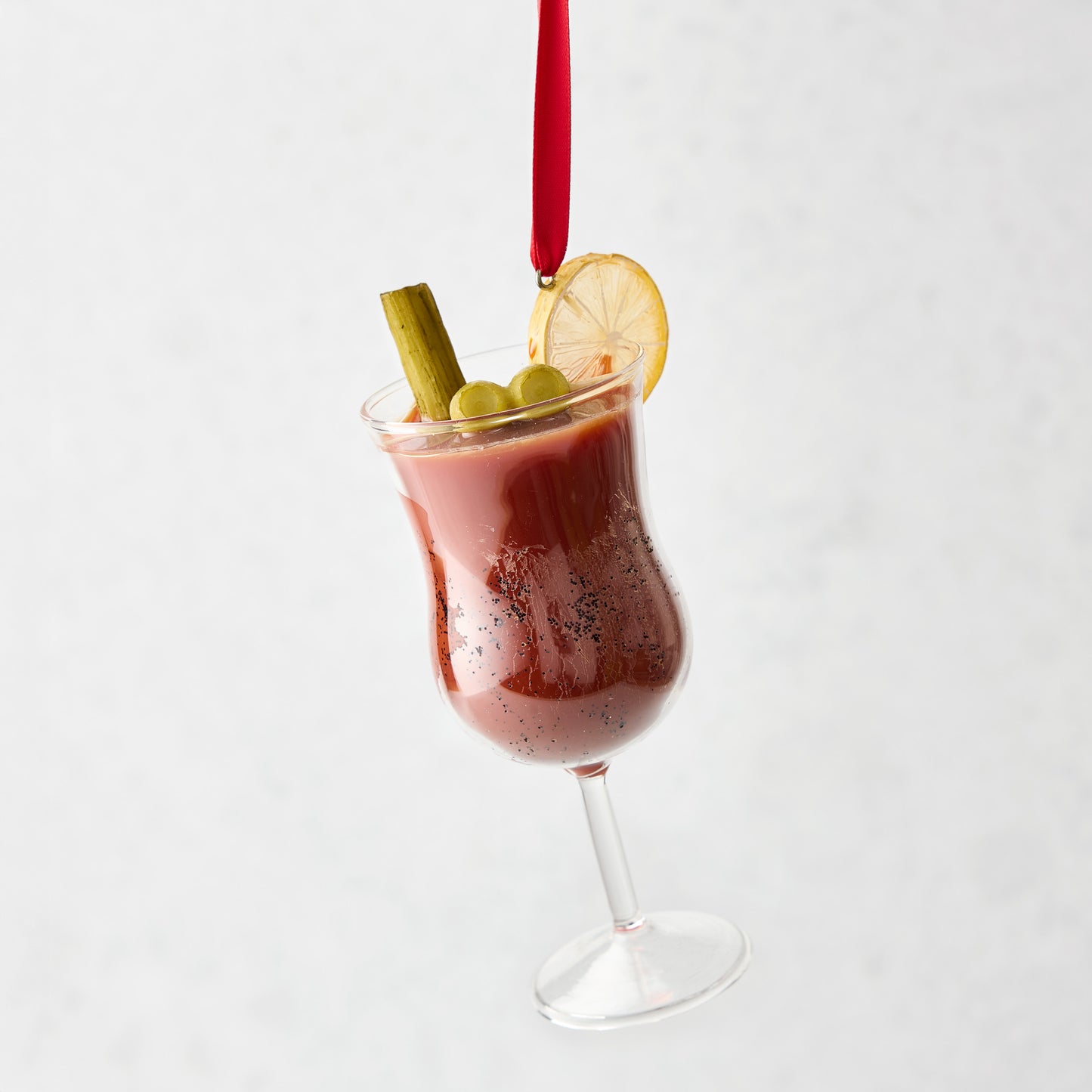 Hand-painted glass Bloody Mary Christmas ornament with celery, olives, and lemon slice garnish on a red ribbon.