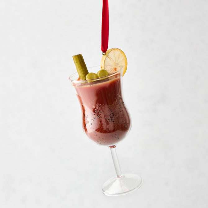 Hand-painted glass Bloody Mary Christmas ornament with celery, olives, and lemon slice garnish on a red ribbon.