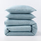 Stacked blue and green striped European washed linen duvet and two shams on a white background.