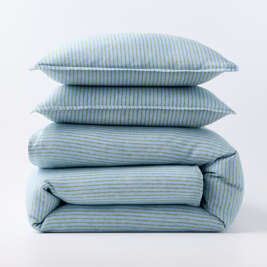 Stacked blue and green striped European washed linen duvet and two shams on a white background.