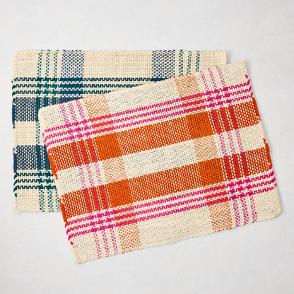 Two rectangular woven abaca and jute placemats: one blue and beige plaid, one orange and pink plaid.