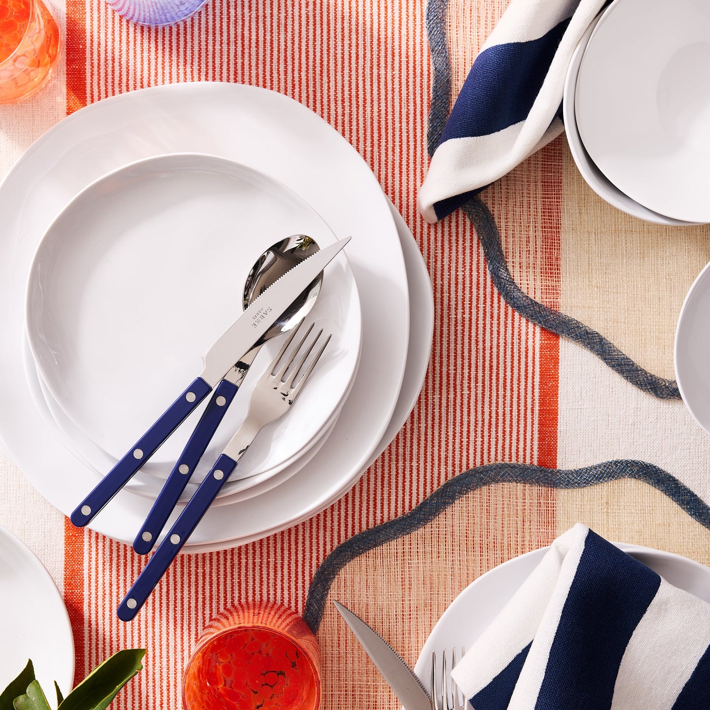 Blue 5-piece stainless steel flatware set with acrylic handles arranged on a white plate and striped table runner.