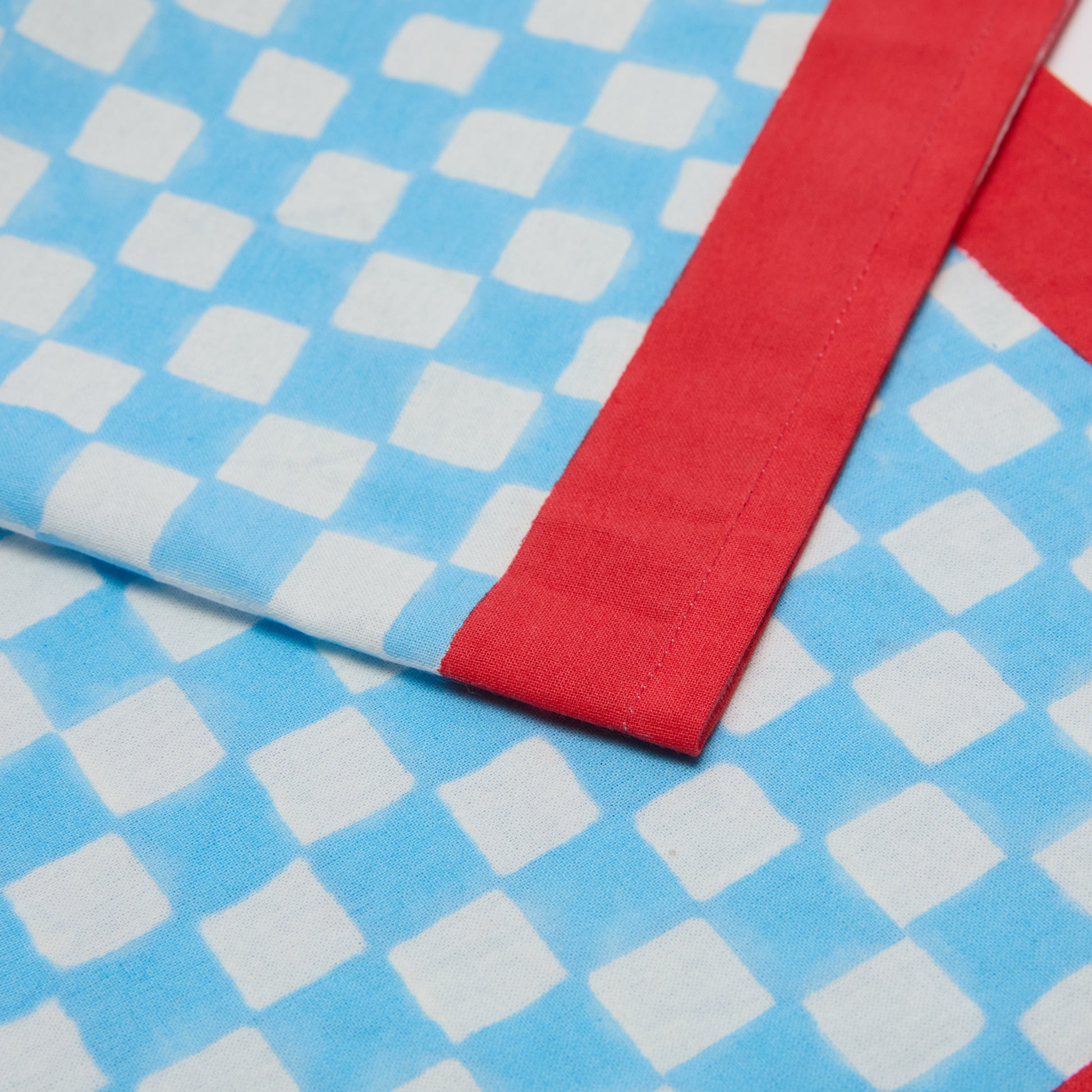 Blue check cotton voile napkin with a red border, 20" square.