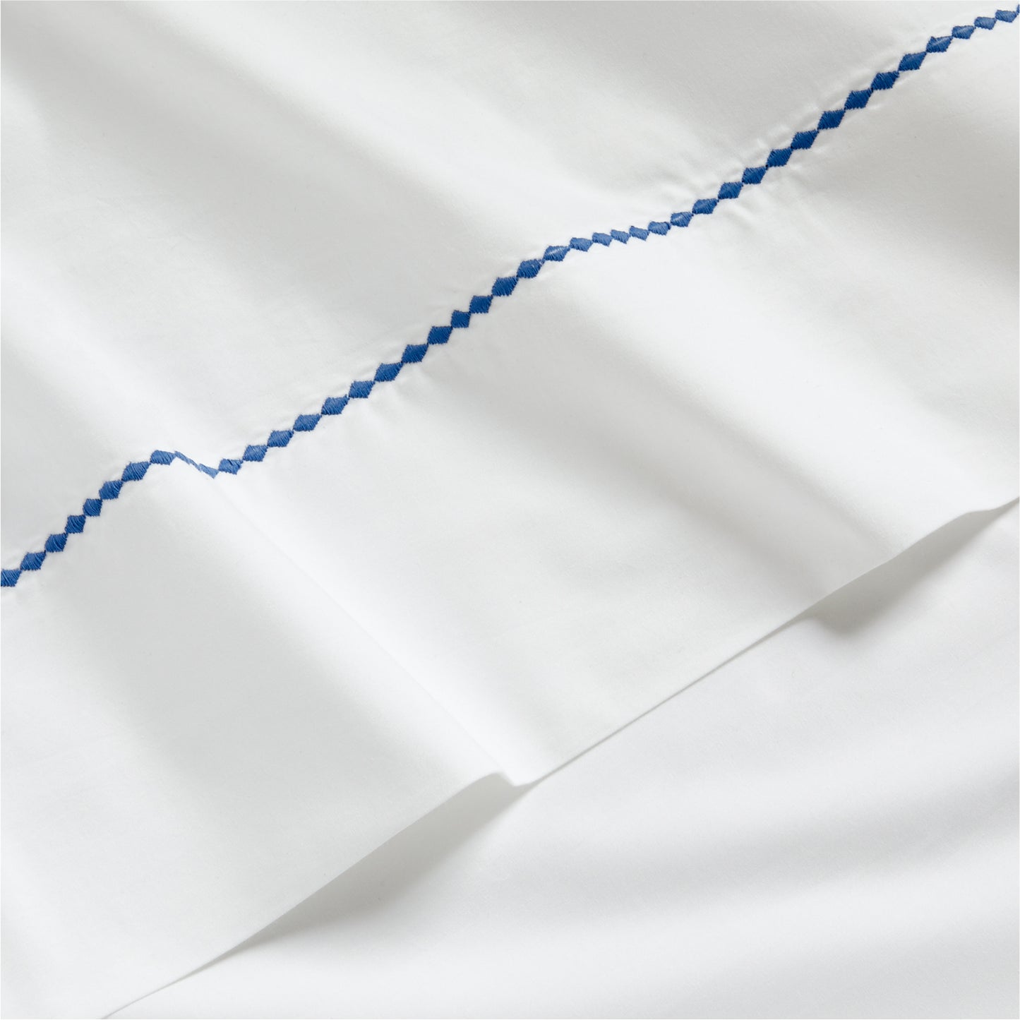 White percale sheet set with a blue diamond embroidered detail.