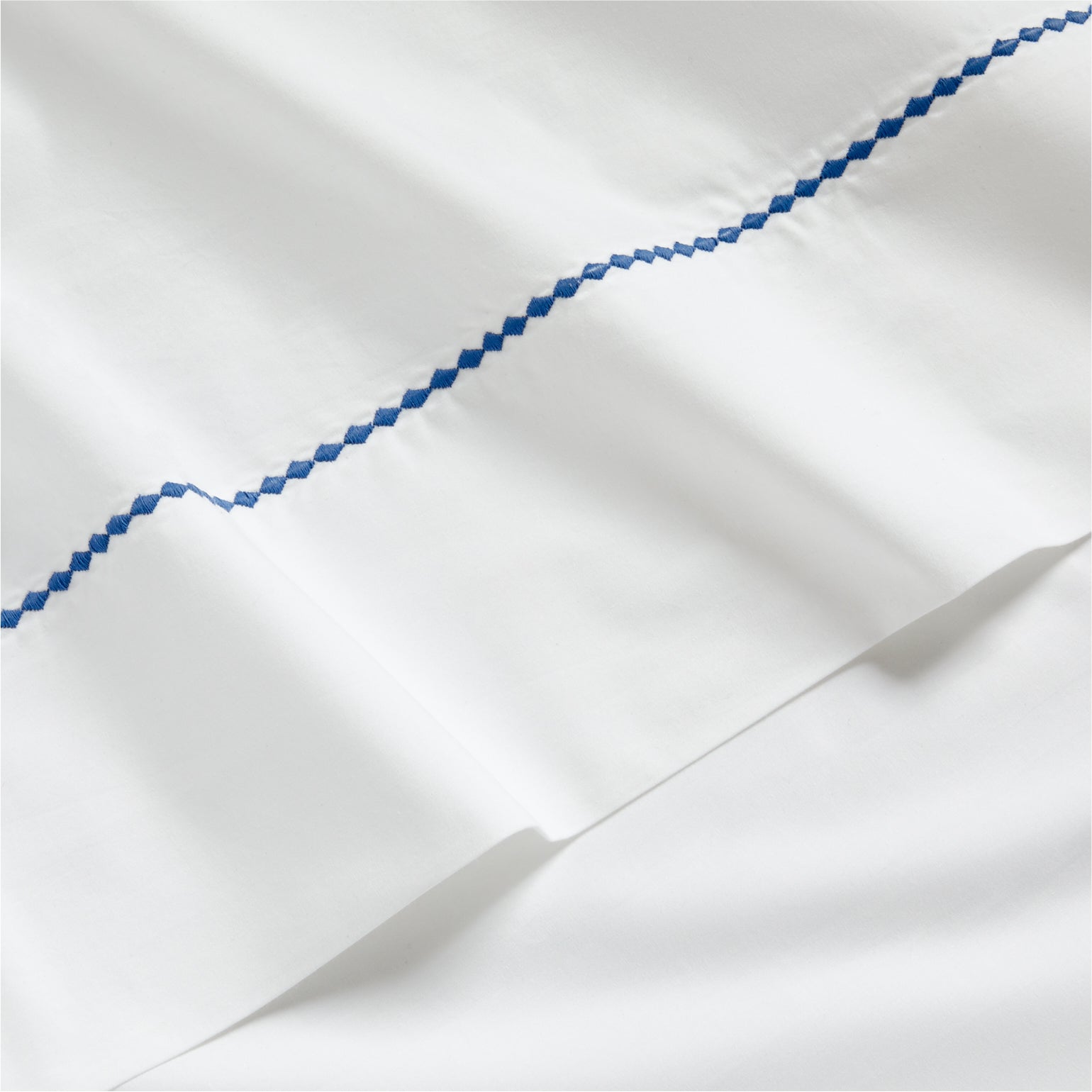 White percale sheet set with a blue diamond embroidered detail.