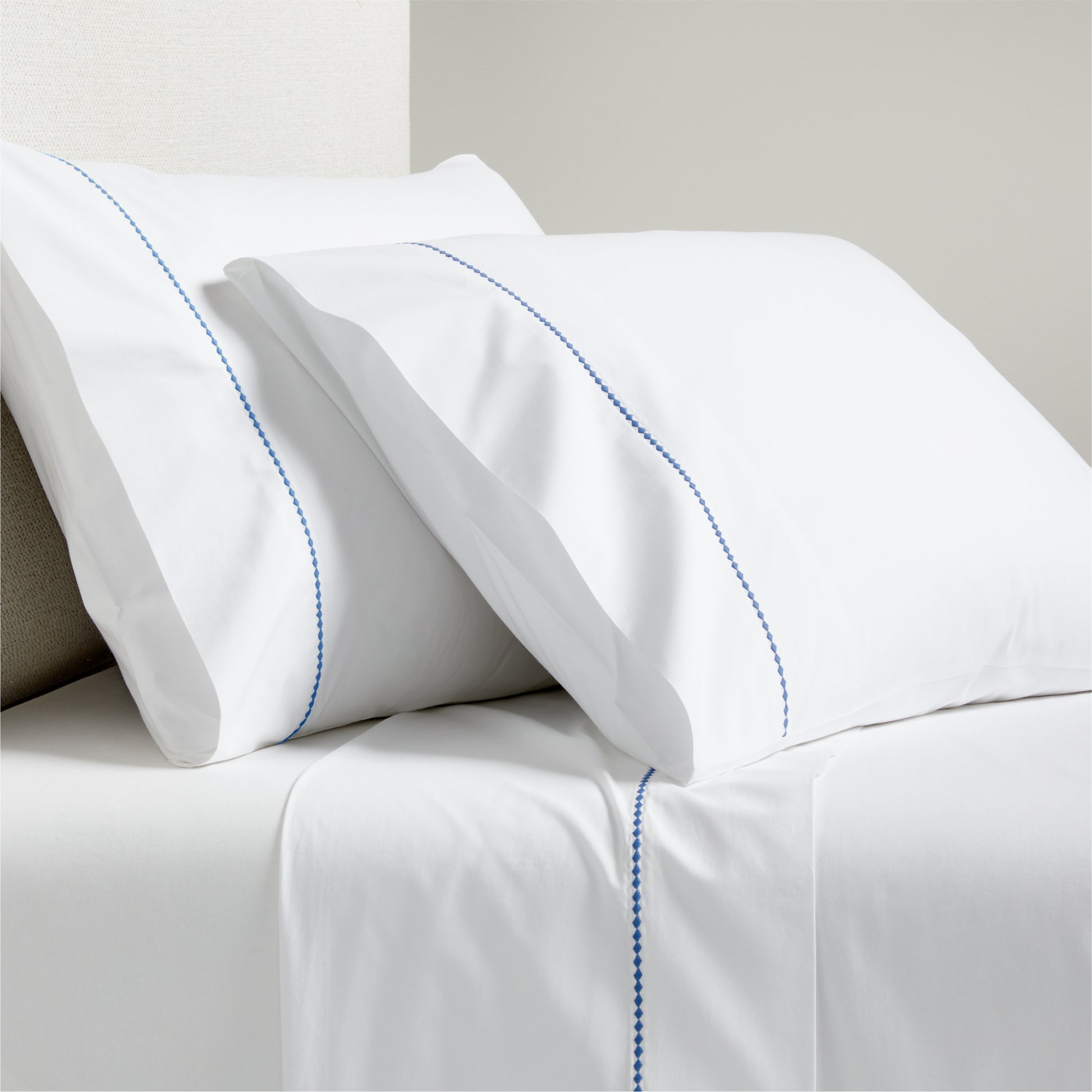 White percale sheet set with blue diamond embroidered detail on pillowcases and flat sheet.