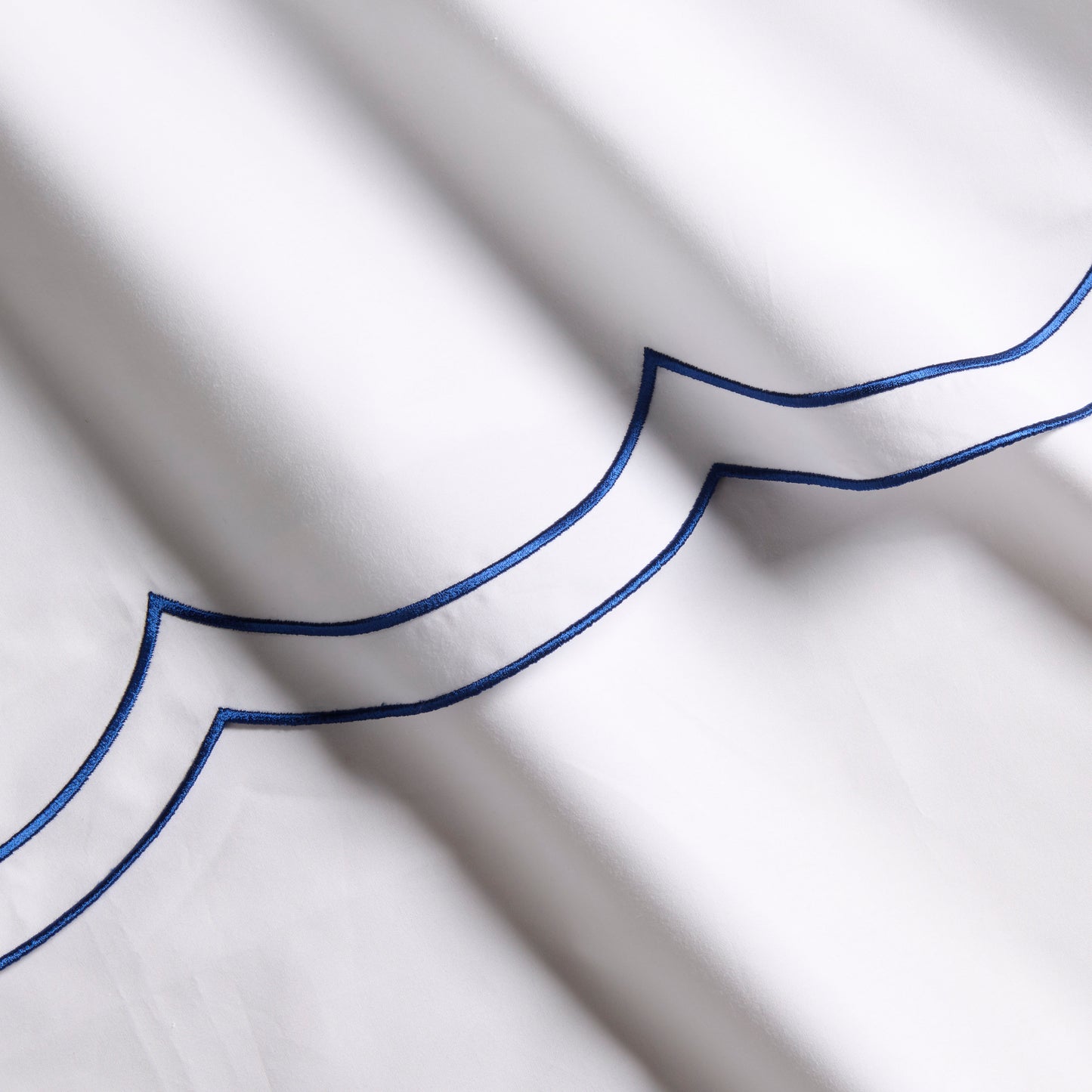 White organic cotton percale sheet with blue double scallop stitch embroidery.