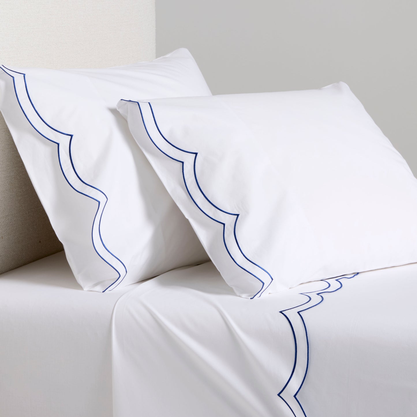 White organic cotton percale sheet set with blue double scallop stitch embroidery on pillows and flat sheet.