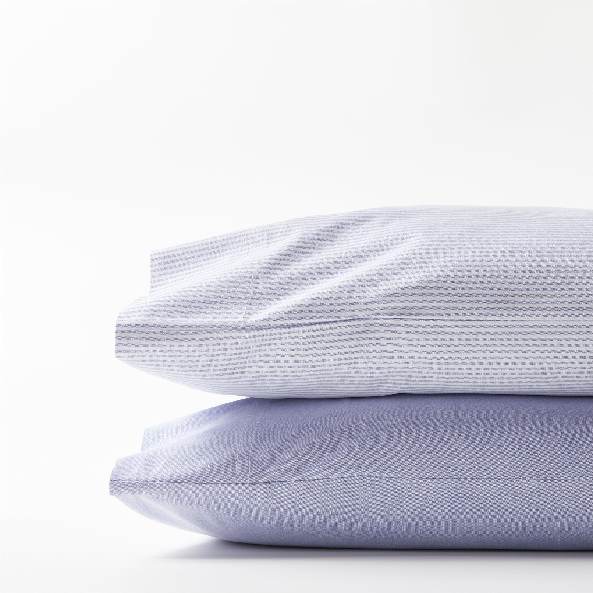Stacked Blue Oxford Stripe and solid blue cotton pillowcases.