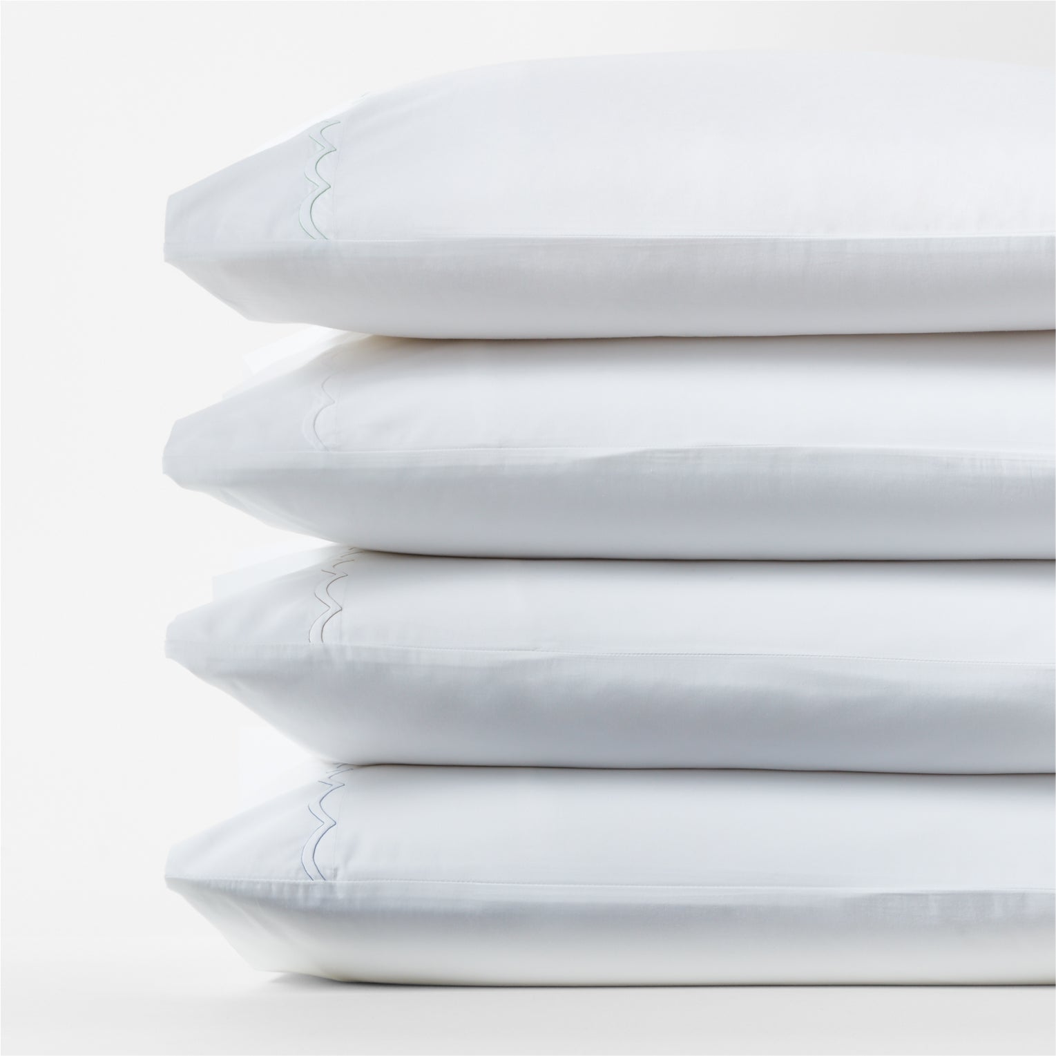 Stack of four white percale pillowcases with blue scallop stitch trim.