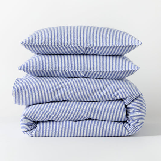 Blue seersucker stripe organic cotton duvet cover and two shams, folded and stacked.