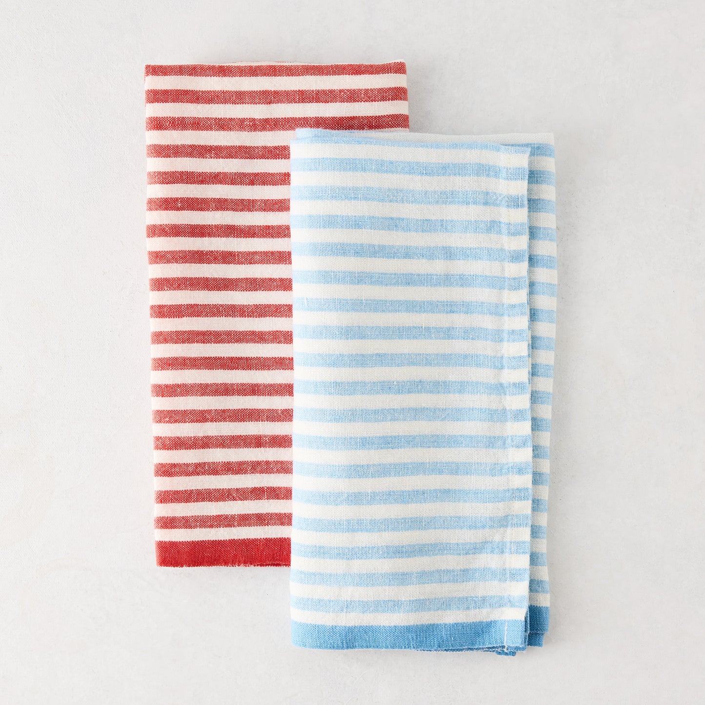 Folded blue and white ticking stripe linen napkin next to a red striped napkin.