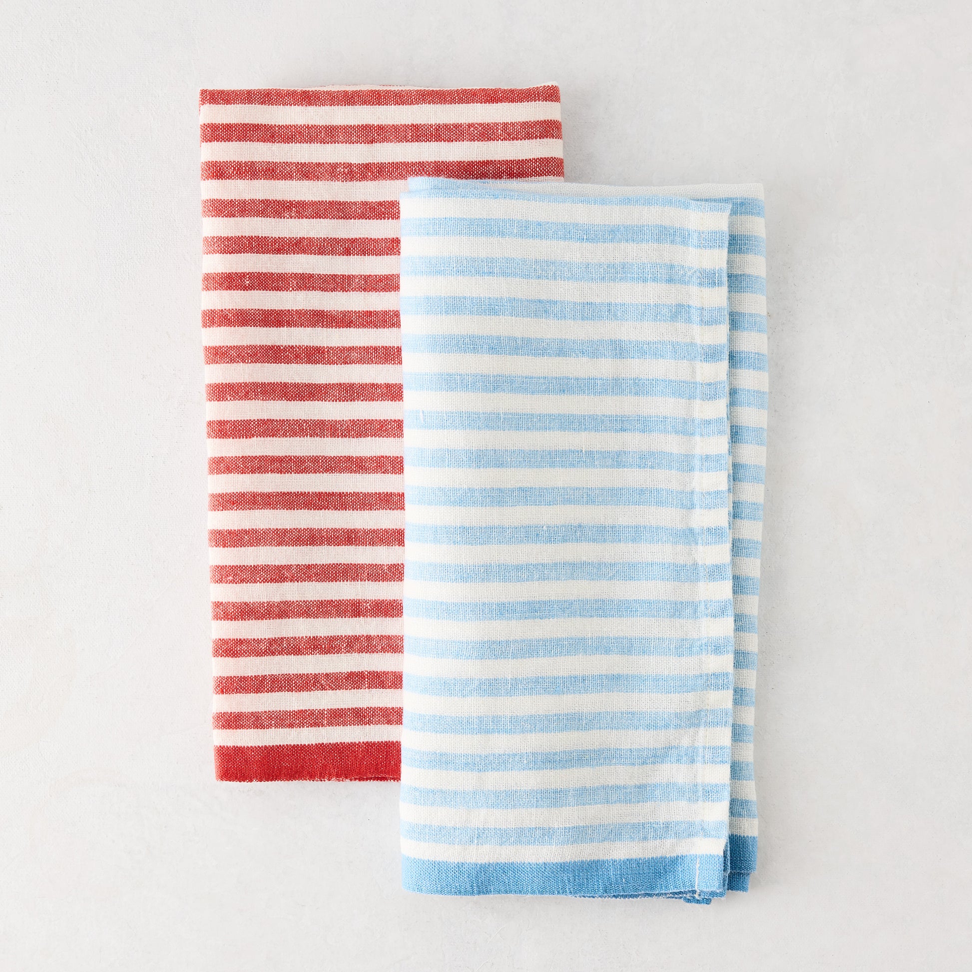 Folded blue and white ticking stripe linen napkin next to a red striped napkin.