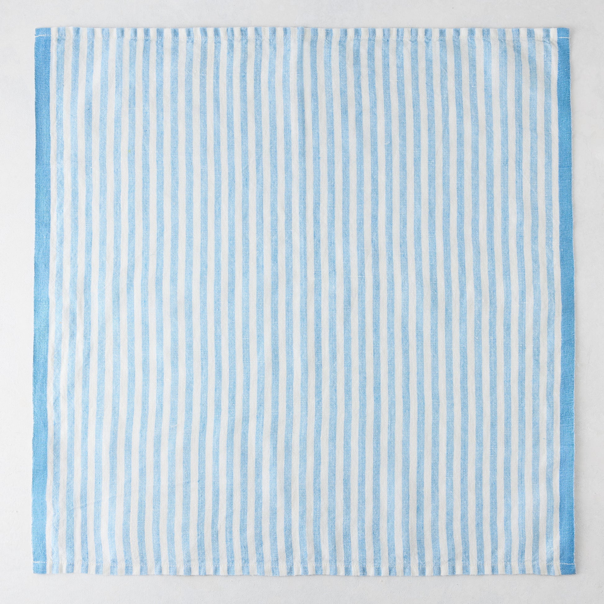 Blue Ticking Stripe Linen Napkin, 21" square, with thin light blue and white vertical stripes and a thicker blue border.