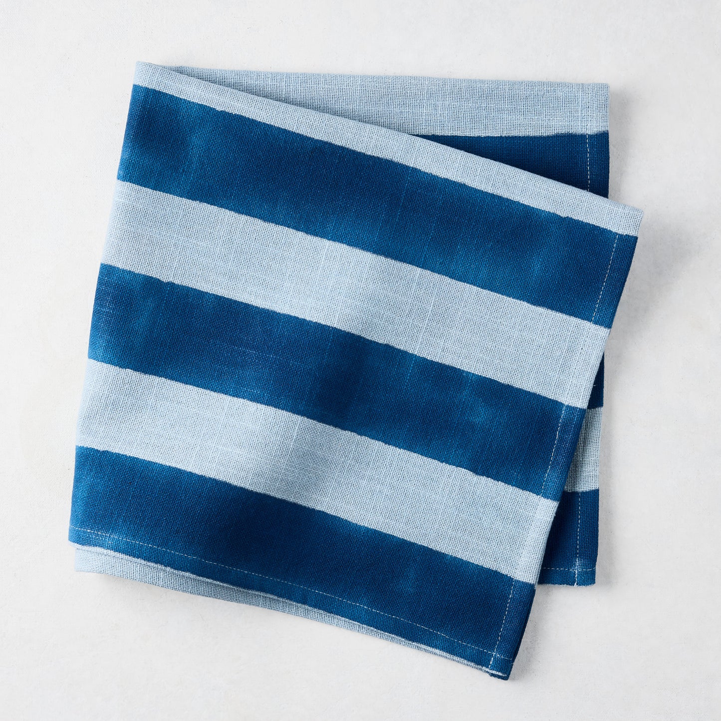 Folded Blue Tonal Hampton Stripe Cotton Napkin with bold and light blue stripes.