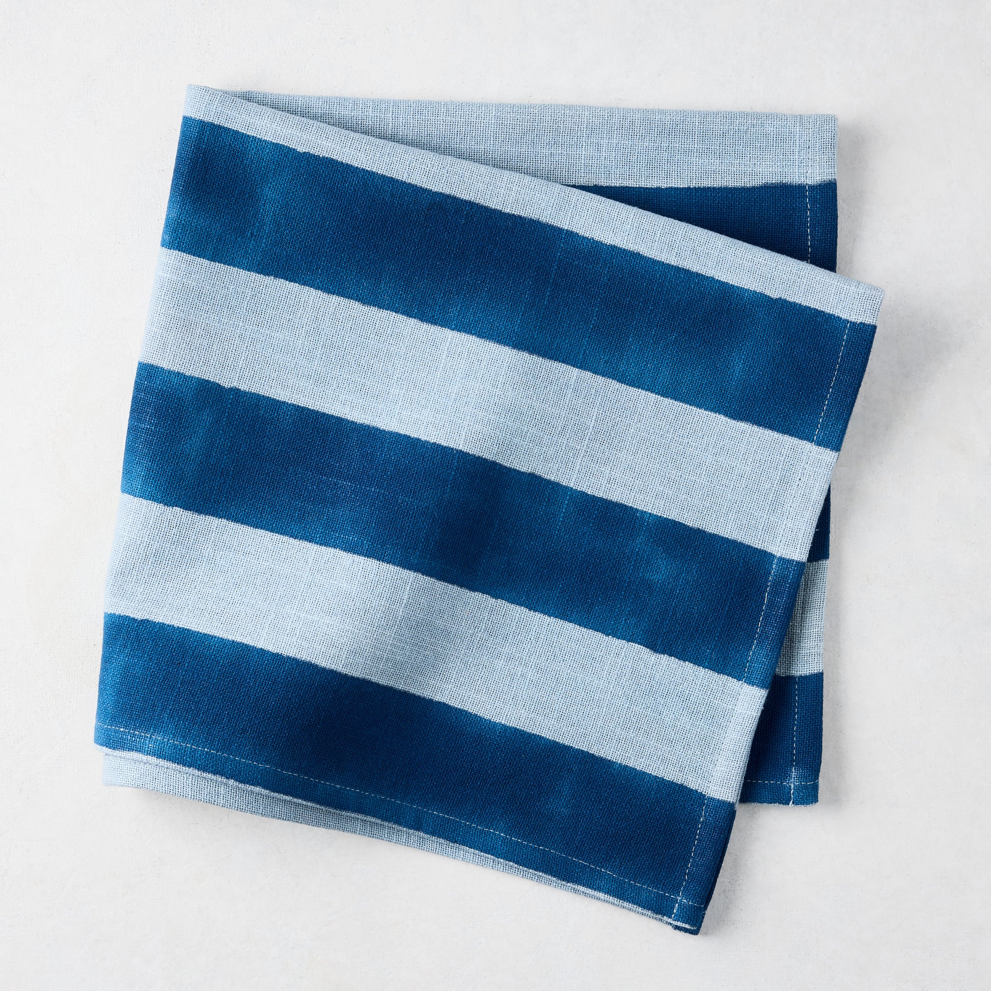 Folded Blue Tonal Hampton Stripe Cotton Napkin with bold and light blue stripes.