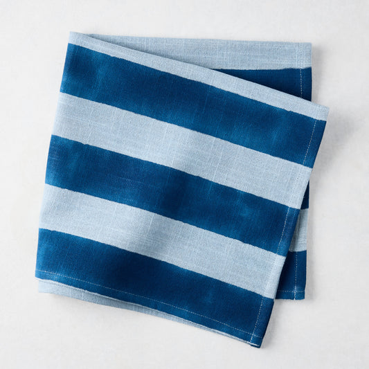 Folded Blue Tonal Hampton Stripe Cotton Napkin with bold and light blue stripes.