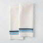 Set of 2 white cotton-linen hand towels with blue triple stripes, folded.