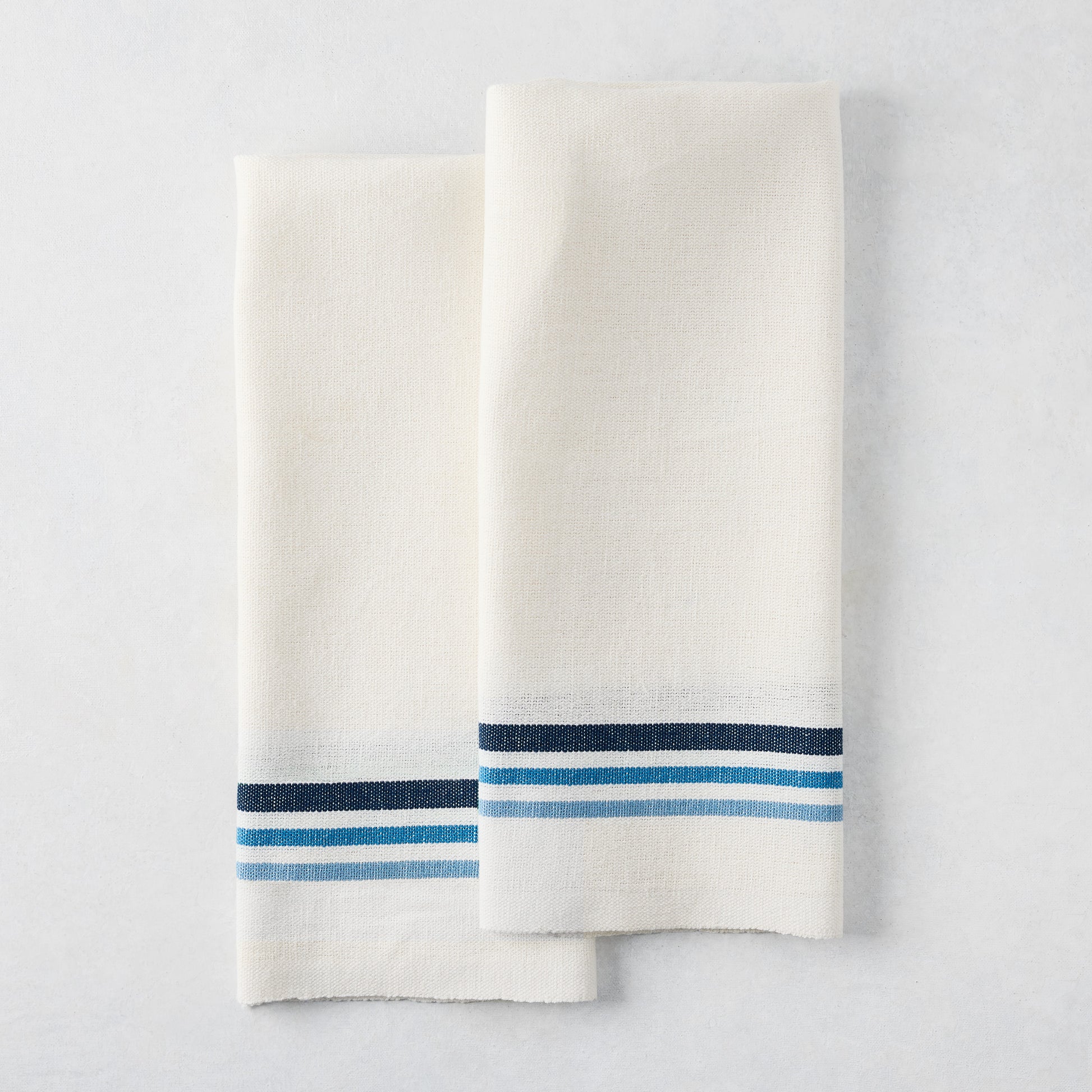 Set of 2 white cotton-linen hand towels with blue triple stripes, folded.