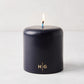 HG Blue unscented 4x4 pillar candle with gold HG logo and lit cotton wick.