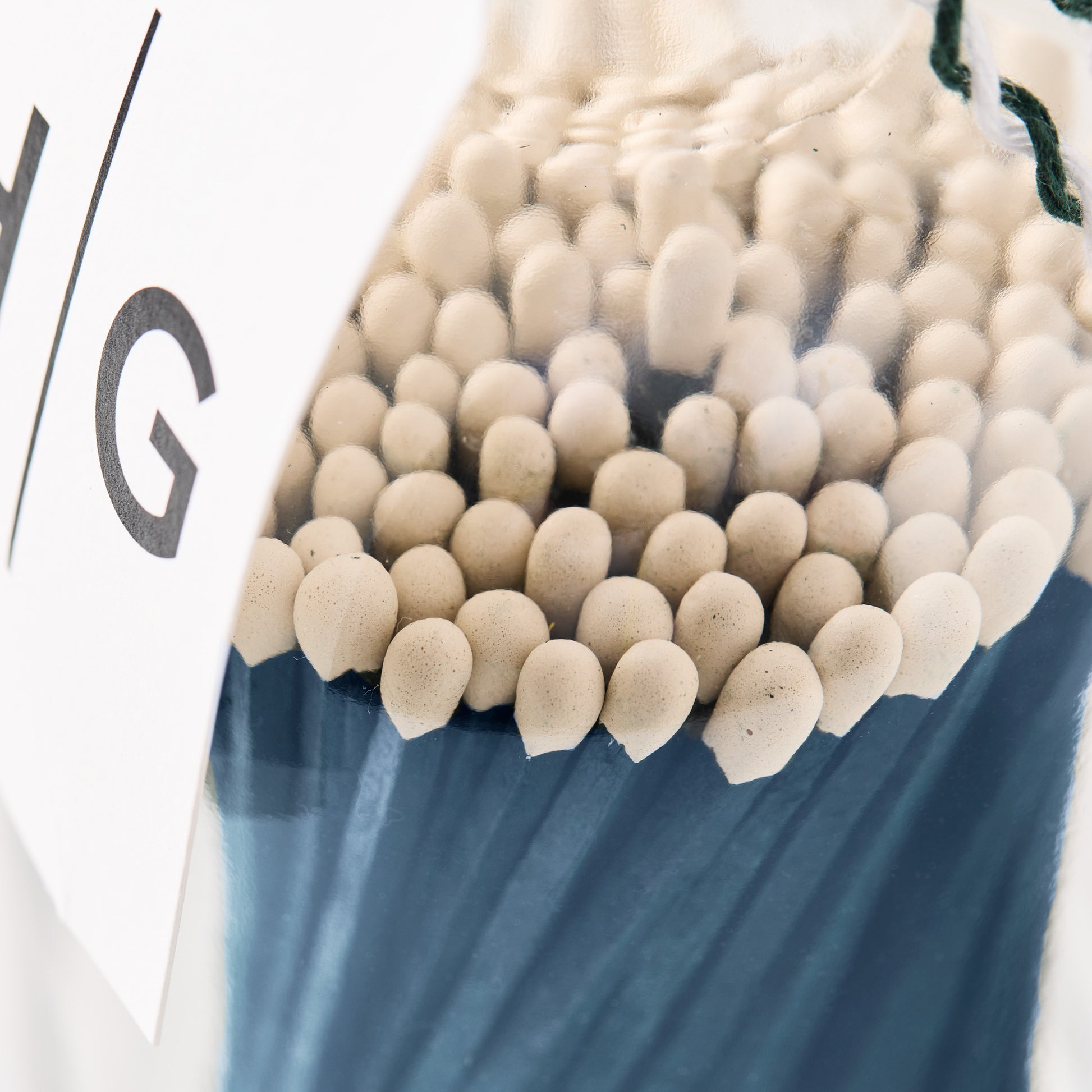 Close-up of blue matches with white tips in a clear glass bottle.