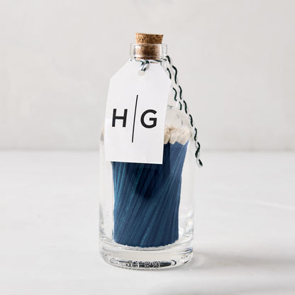 Blue with white tip oversized matches in a glass bottle with cork stopper and "HG" tag.