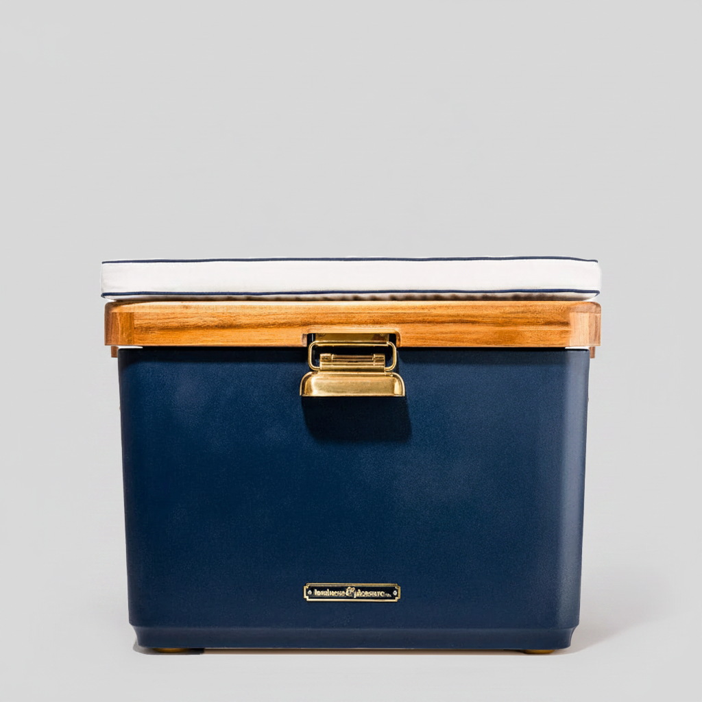 Navy blue 55-quart Hemingway cooler with acacia wood lid, white cushion, and stainless steel latch on gray background.