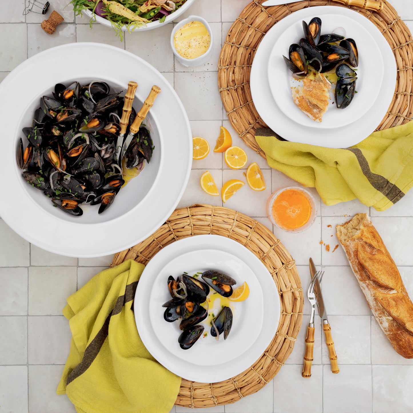 White Bolinas Round Ceramic Serve Bowl with Trim filled with mussels, surrounded by plates and food.