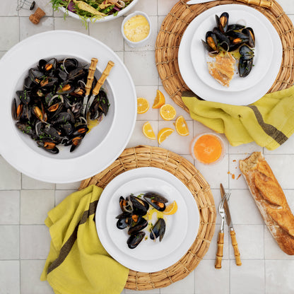 White Bolinas Round Ceramic Serve Bowl with Trim filled with mussels, surrounded by plates and food.