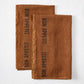 Two folded brown linen hand towels with "BON APPETIT" printed in black.