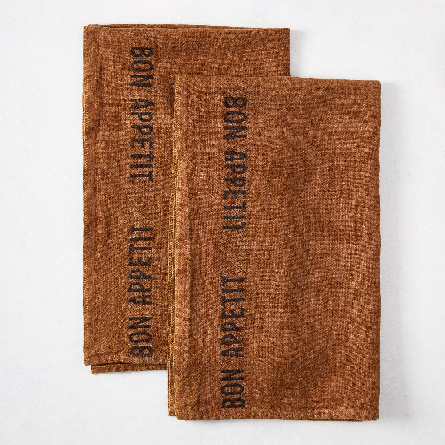 Two folded brown linen hand towels with "BON APPETIT" printed in black.
