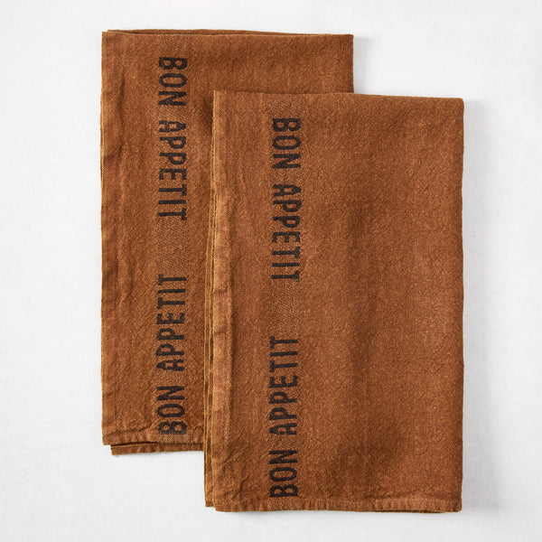 Two folded brown linen hand towels with "BON APPETIT" printed in black.