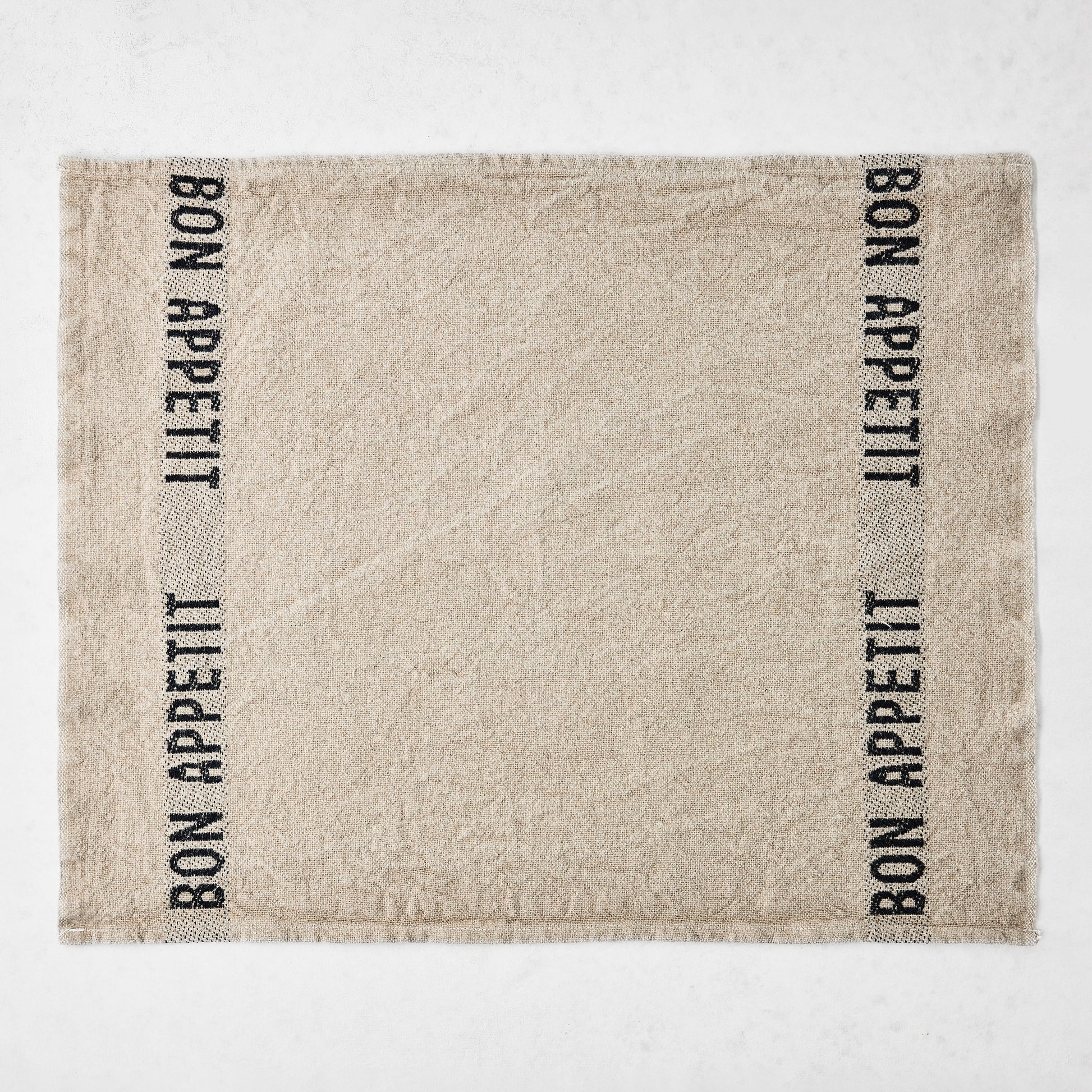 Camel khaki linen napkin with "BON APPETIT" in black lettering on two vertical stripes.