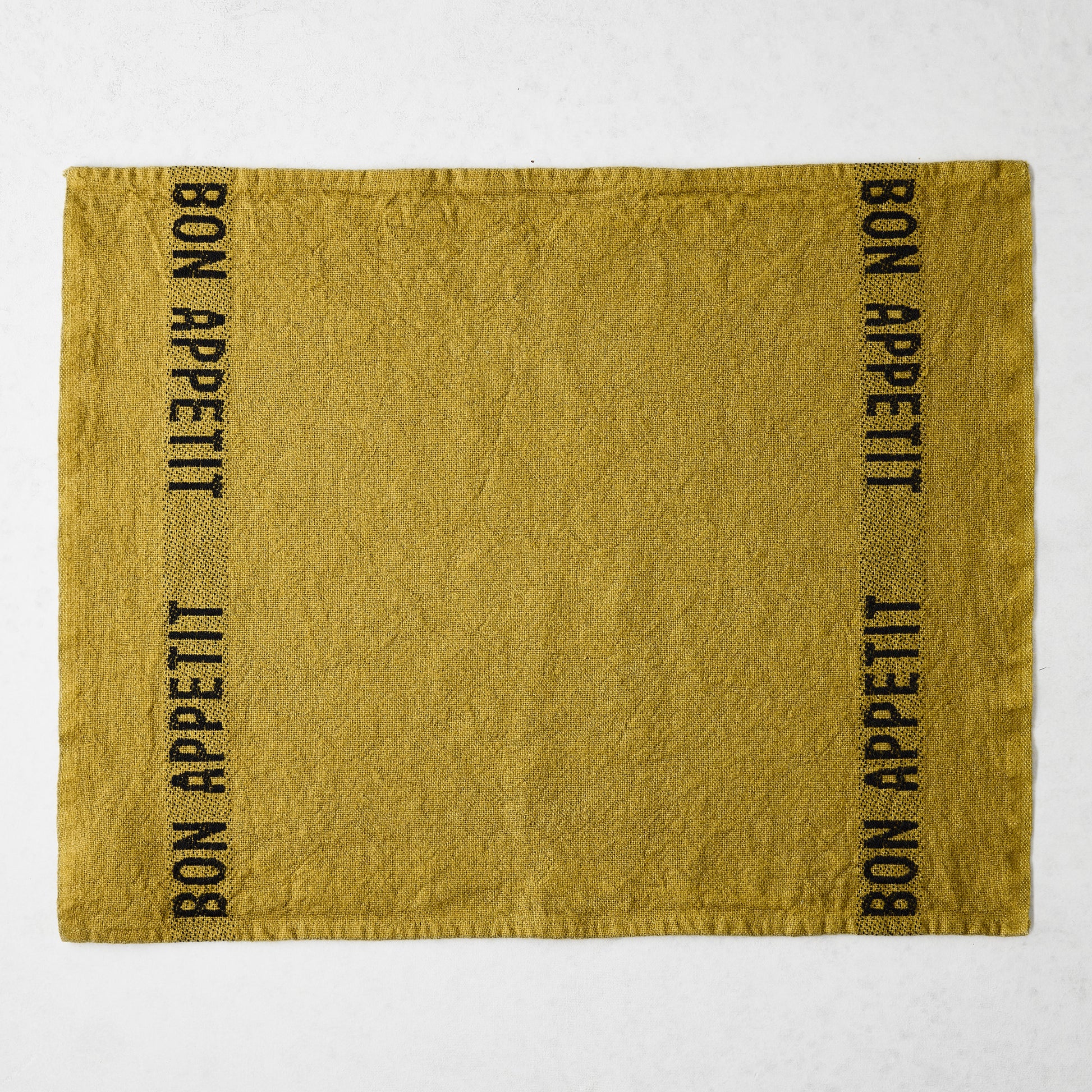 Goldenrod linen napkin with "BON APPETIT" in black text on two vertical sides.
